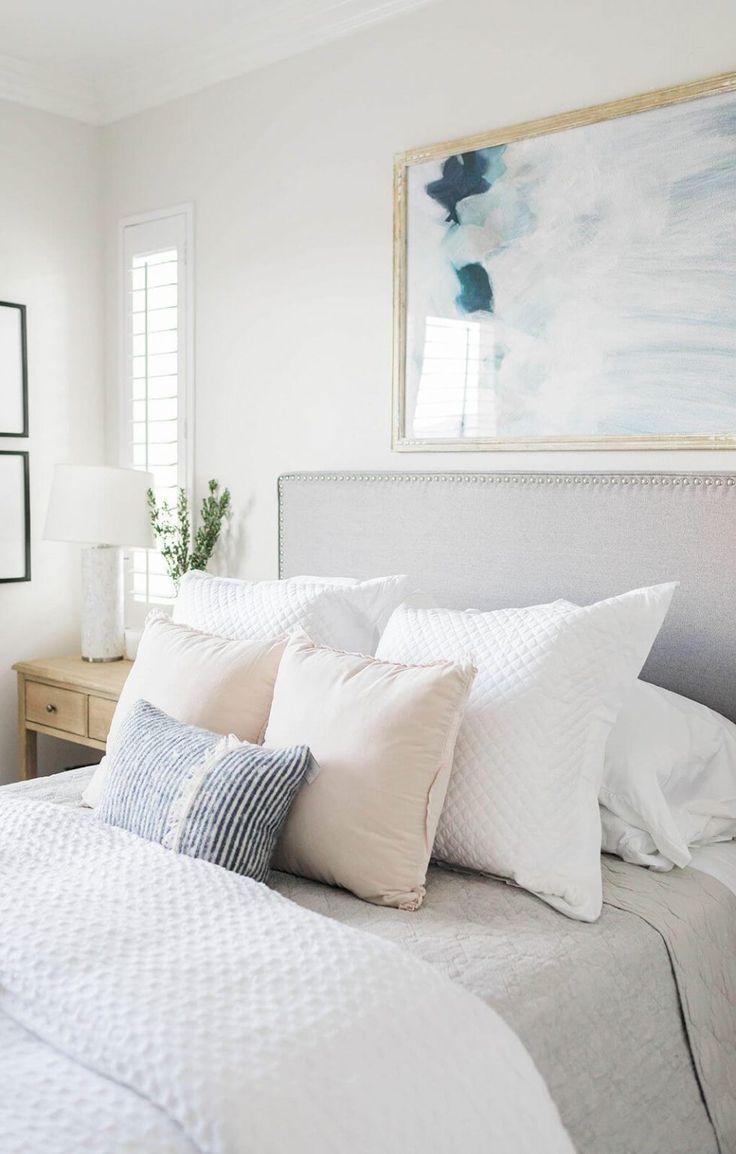 a bed with white linens and pillows in a small room next to a painting on the wall