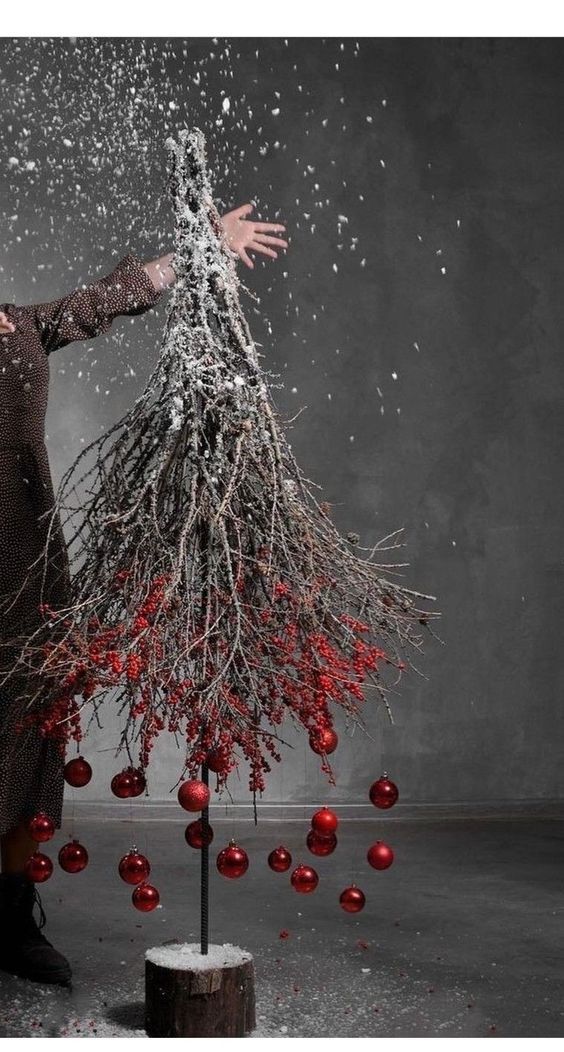 a woman standing in front of a christmas tree with red ornaments on it's branches