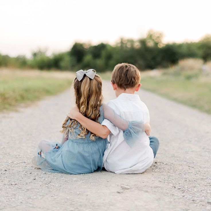 two young children sitting on the side of a dirt road looking at something in the distance