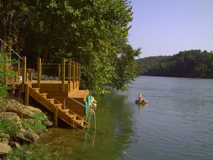 two people in a small boat on the water next to a dock and some trees