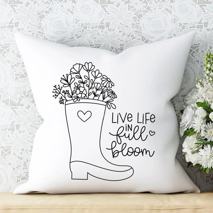 a white pillow sitting on top of a wooden table next to a vase with flowers