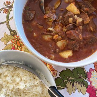 a bowl of stew and rice on a colorful tablecloth with a spoon in it