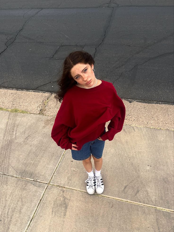 a woman standing on the sidewalk with her hands in her pockets and looking at the camera