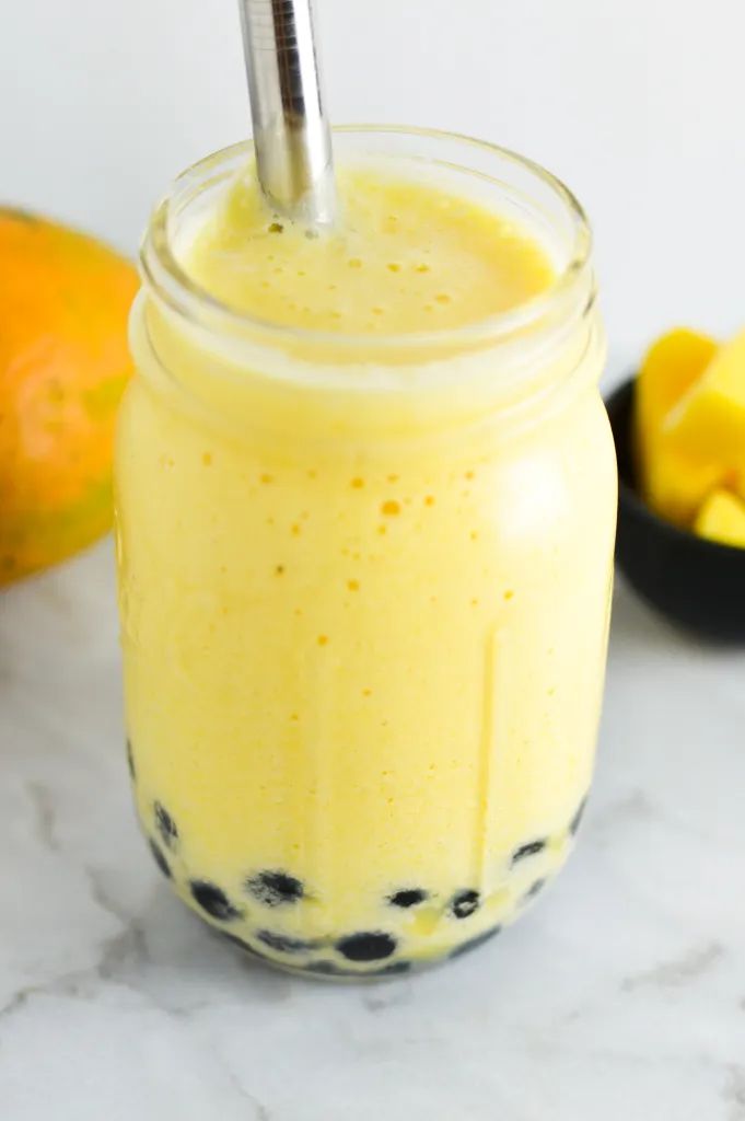 a smoothie in a mason jar with a straw sticking out of the top and mangoes around it