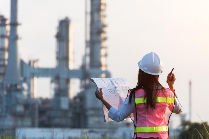 a woman in safety vest and hard hat looking at an oil refinery