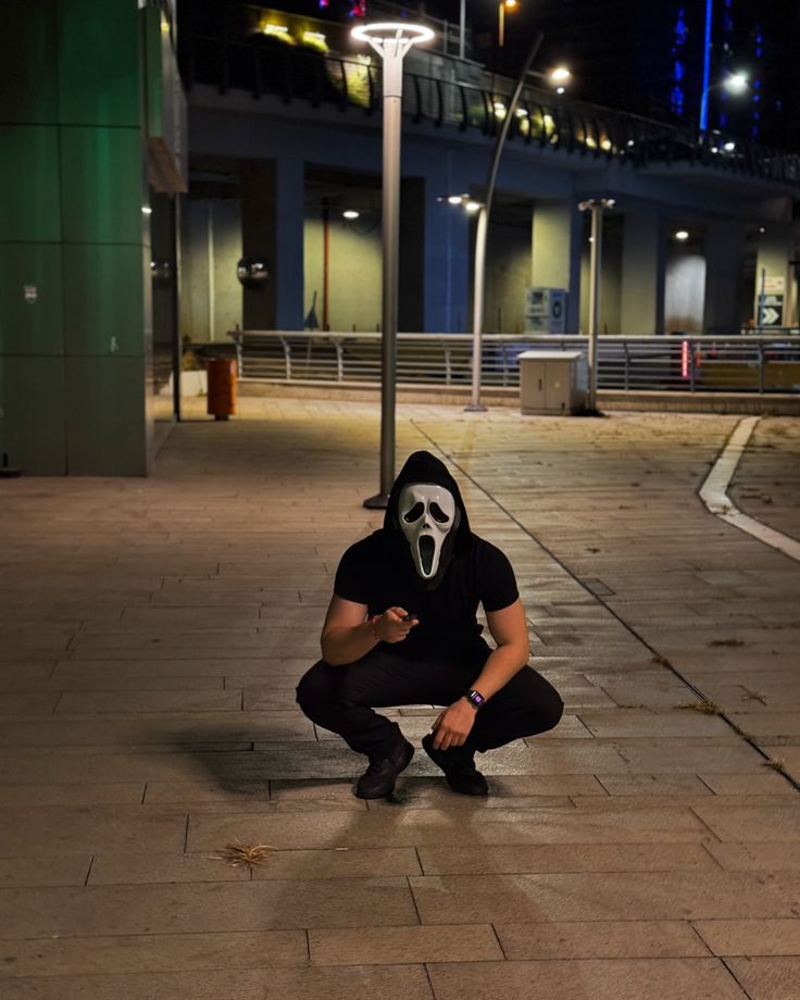 a man in a mask squatting down on the sidewalk