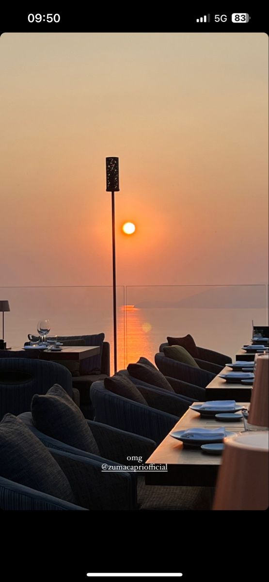 the sun is setting over the ocean with tables and chairs