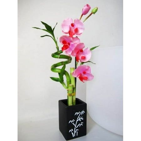 pink flowers are in a black vase with bamboo stems on the bottom and white wall behind it