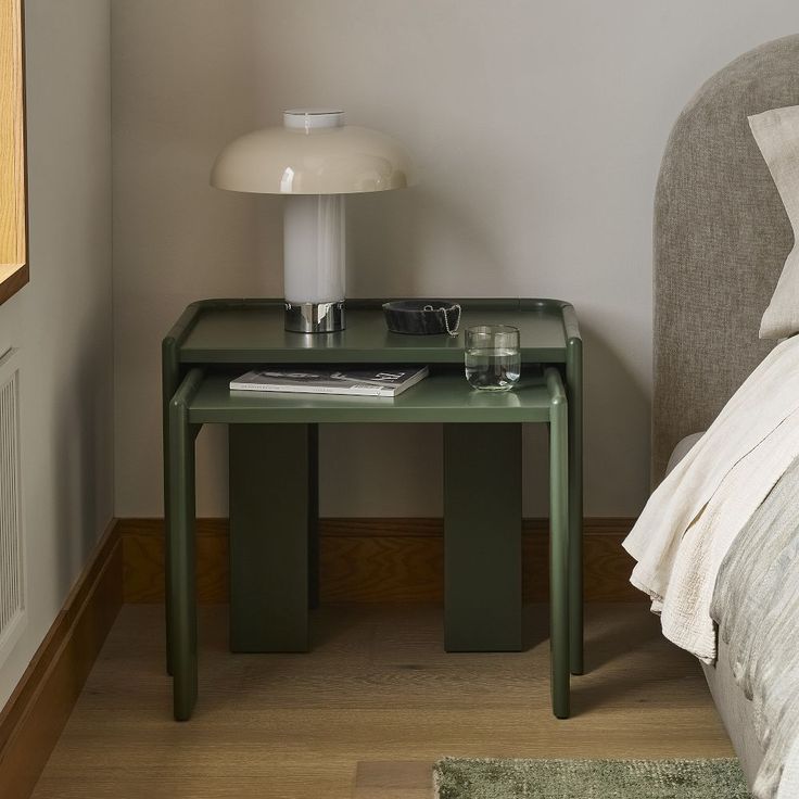 a small green table sitting on top of a wooden floor next to a white bed