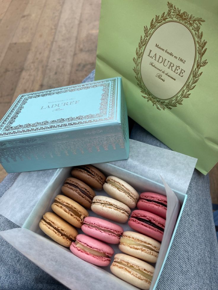 a box filled with lots of different flavored macaroons next to a paper bag