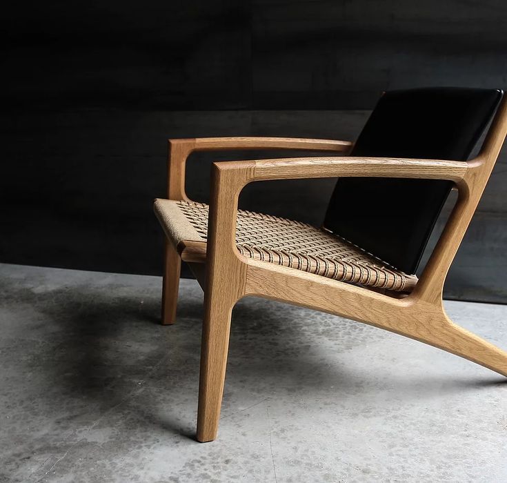 a wooden chair sitting on top of a cement floor next to a black leather cushion