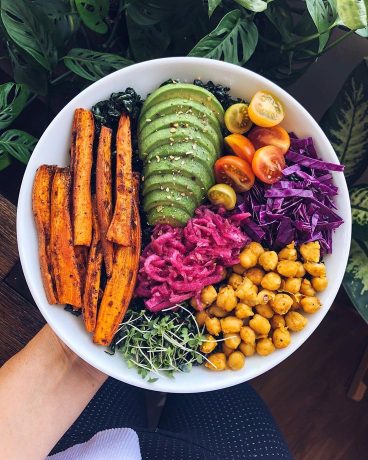 a white bowl filled with different types of food on top of a wooden table next to plants