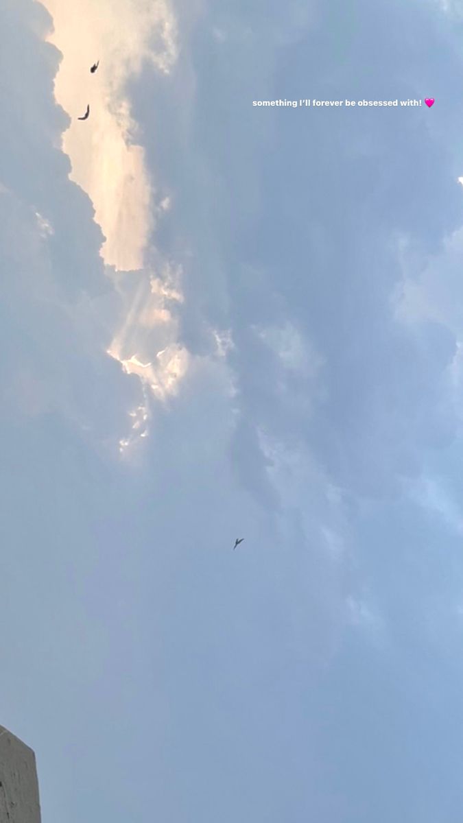 two kites flying in the sky on a cloudy day with sun peeking through clouds