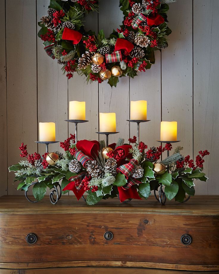 a christmas centerpiece with pine cones, holly wreaths and candles in front of a wooden wall