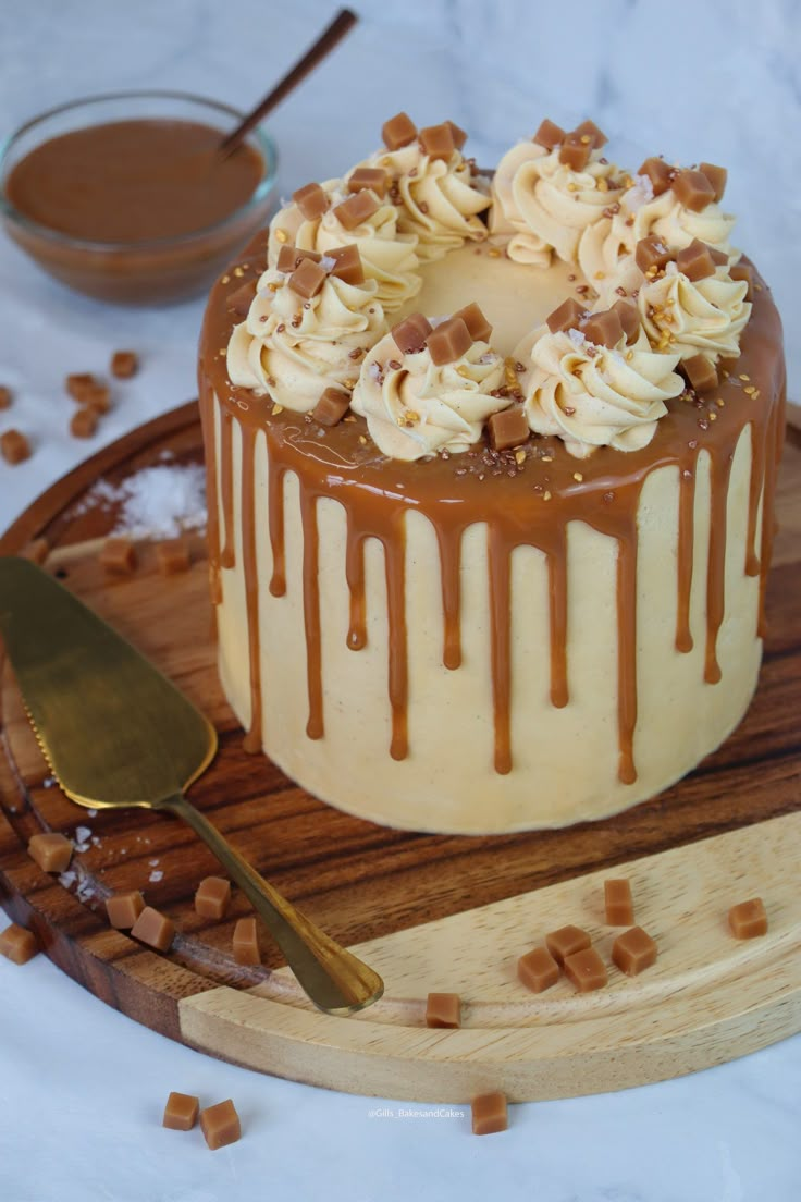 a cake with white frosting and caramel toppings on a wooden platter