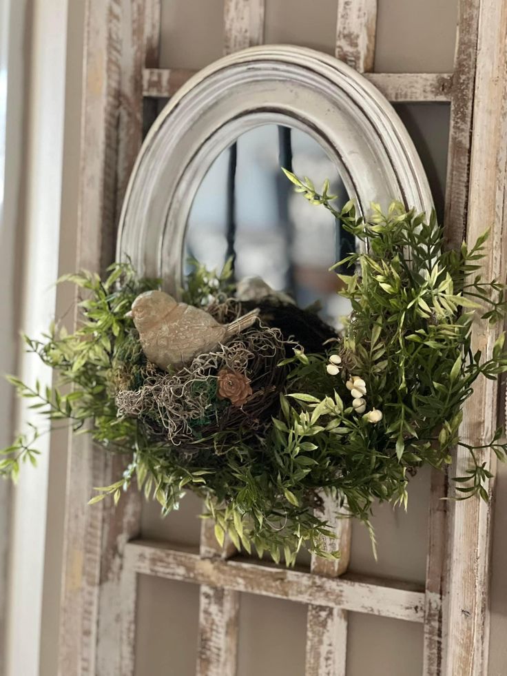 an old window frame is decorated with greenery and a bird's nest in the center