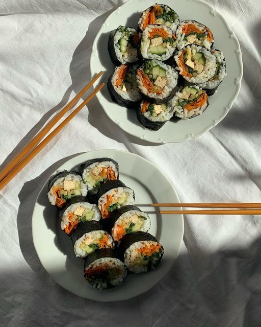 two plates filled with sushi and chopsticks on top of a white table cloth