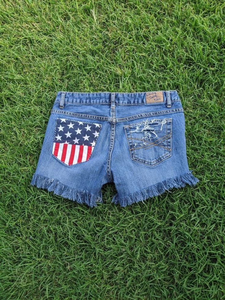 "Cutoff shorts, US Flag print fabric hand sewn over pocket with embroidery thread, frayed edges, long fringe at bottom, Studded.   Measurements taken flat in inches:  Waist/or across top 15 (30 around top) top to bottom between 11 and 12 inseam between 2 inches including fringe front rise 8 hips near bottom of zipper is about 17  (34 around). *Full body model is 32,24,34 and 5'6\" and the curvy model is 23 waist and 37-38 hips to compare fit. Always smoke-free.  If I've missed something please ask!   Find me on Instagram, Google+ Twitter or Pheed at  jennifer_pace Thank you! Jennifer" Festival Cutoff Jean Shorts With Frayed Hem, Short Cotton Bottoms With Patches, Distressed Cutoff Bottoms For Festival, Cutoff Cotton Shorts For 4th Of July, Cotton Cutoff Shorts For 4th Of July, Festival Shorts With Frayed Hem, Summer Cutoff Shorts With Patches, Frayed Hem Festival Shorts, Summer Cutoff Jean Shorts With Patches