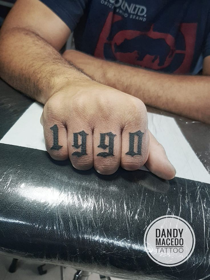 a man with tattoos on his fingers sitting in front of a black object and holding onto the wrist