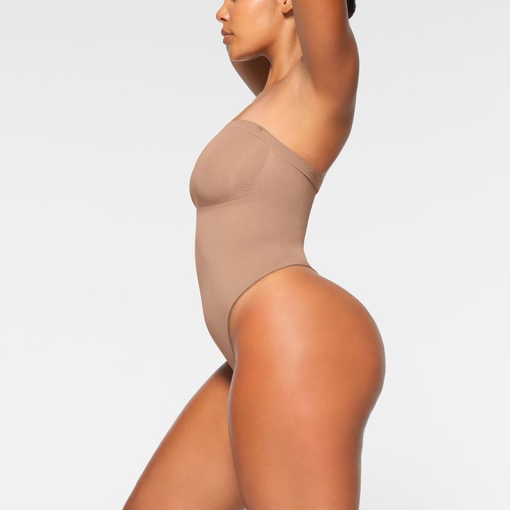 Cinch your waist and sculpt your tummy and core in this perfectly compressive strapless thong bodysuit. Wear it your way with removable adjustable straps that convert to shoulder straps, cross-back, or halter-style. Features center front and side stitching to define and support your bust, and a cotton gusset with snap closure. Fits true to size. | SKIMS Strapless Thong Bodysuit | Medium Neutral | Seamless Sculpt High Cut Nylon Bodysuit With Built-in Bra, Second-skin Bodysuit With Spaghetti Straps And Built-in Bra, Strapless Shaping Bodysuit With Built-in Bra, Sculpting Backless Swimwear With Built-in Bra, Solid Color Bandeau Shapewear, Stretch Bodysuit With Built-in Bra And High-cut Leg, Second-skin Shapewear With Built-in Bra And Full Coverage, Strapless Seamless Shapewear, Smoothing Bandeau Style Shapewear