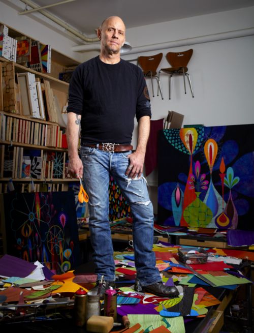 a man standing in an art studio with his hands on his hips and looking at the camera