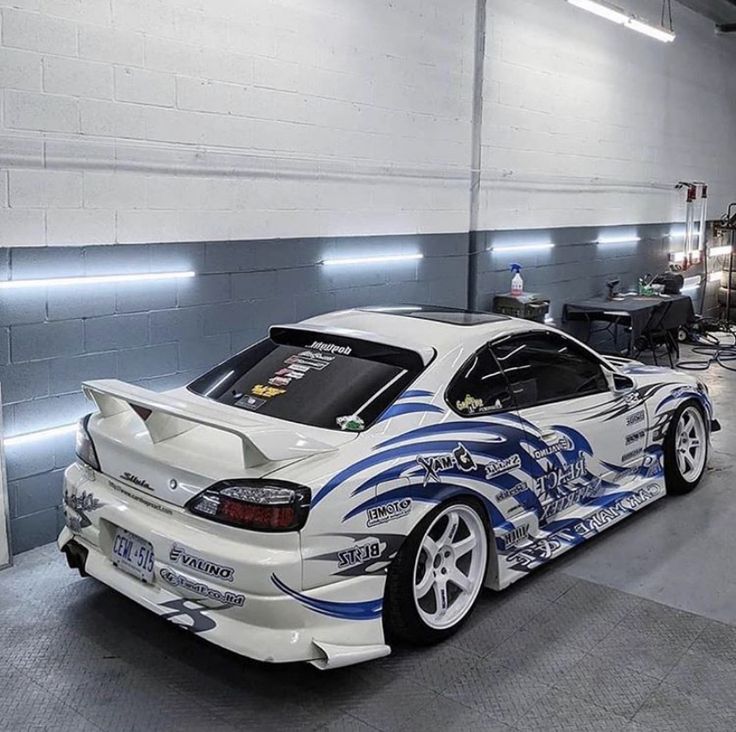 a white sports car with blue flames painted on it's side in a garage