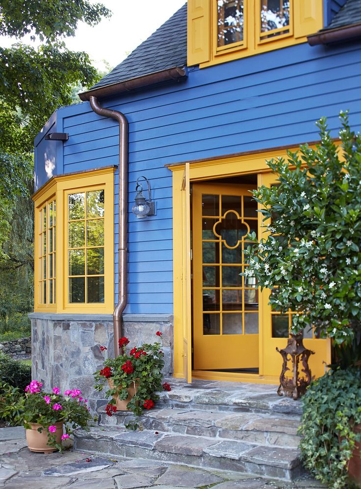 a blue house with yellow doors and flowers on the front steps in front of it