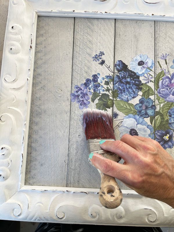 a person holding a paintbrush in front of a flower painting on a wooden frame