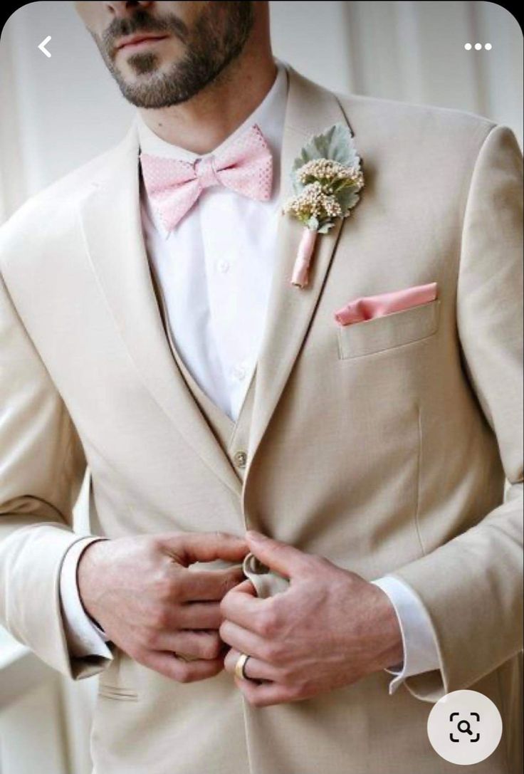 a man in a tan suit with a pink bow tie and boutonniere