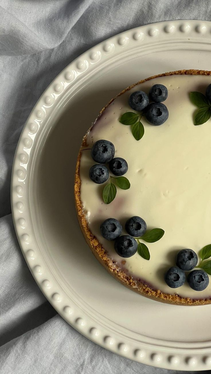 a cheesecake topped with blueberries and mint leaves on top of a white plate