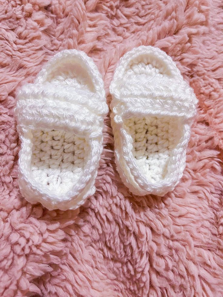 a pair of crocheted baby shoes laying on top of a pink fuzzy blanket