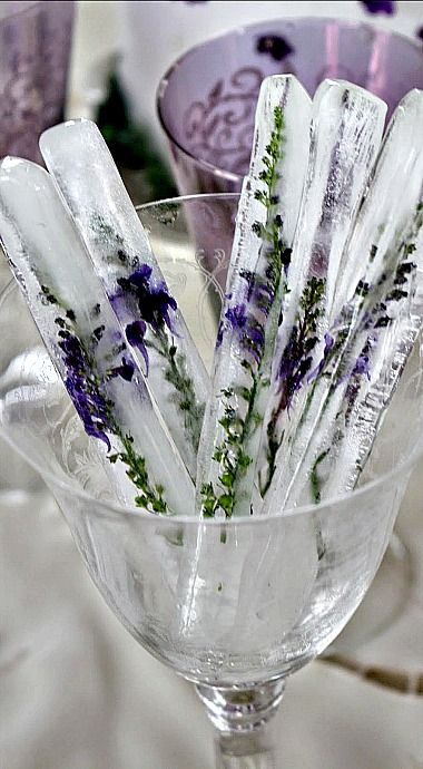 there are some ice sticks in the glass cup on the table with purple and white flowers