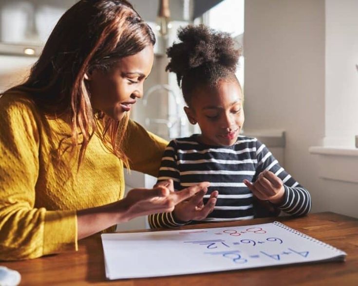 a woman and child sitting at a table looking at a piece of paper with numbers on it