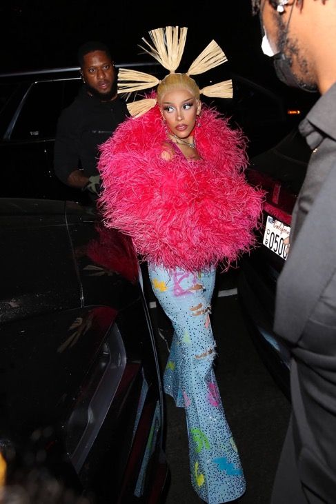 lady in pink and blue outfit standing next to a car at night with man looking on