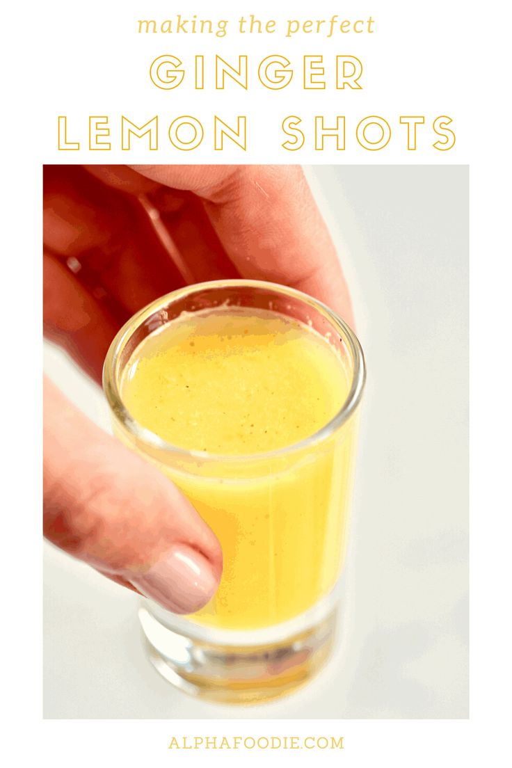 a hand holding a glass filled with orange juice and the words, creating the perfect ginger lemon shots