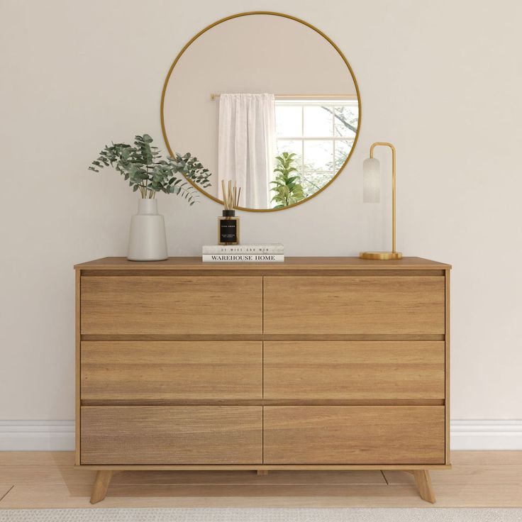 a wooden dresser with a round mirror above it and plants in vases on top