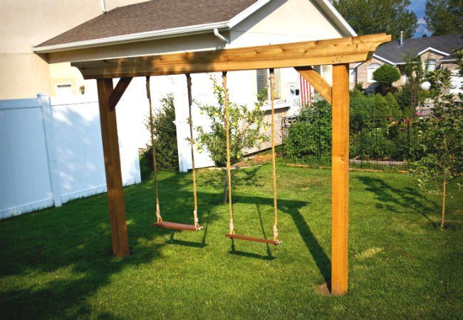 a wooden swing set sitting on top of a lush green field next to a house