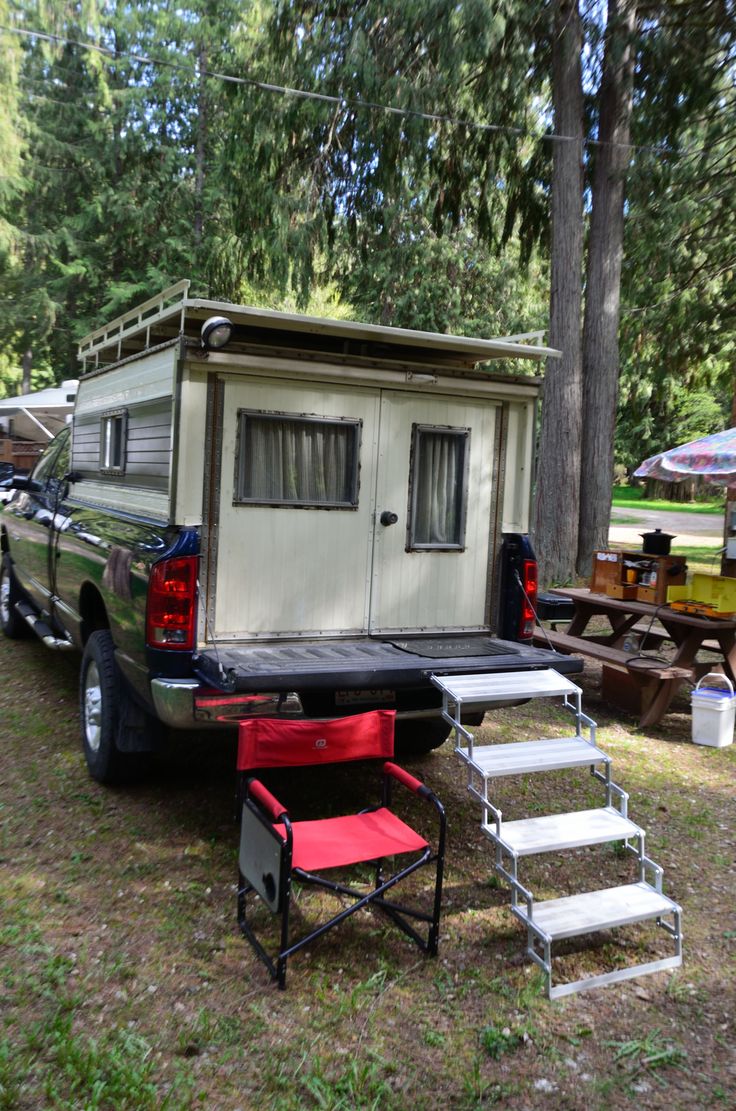 a truck with a camper attached to it parked in the grass next to trees