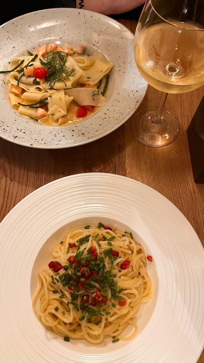 two plates of pasta and wine on a wooden table with glasses of wine in the background