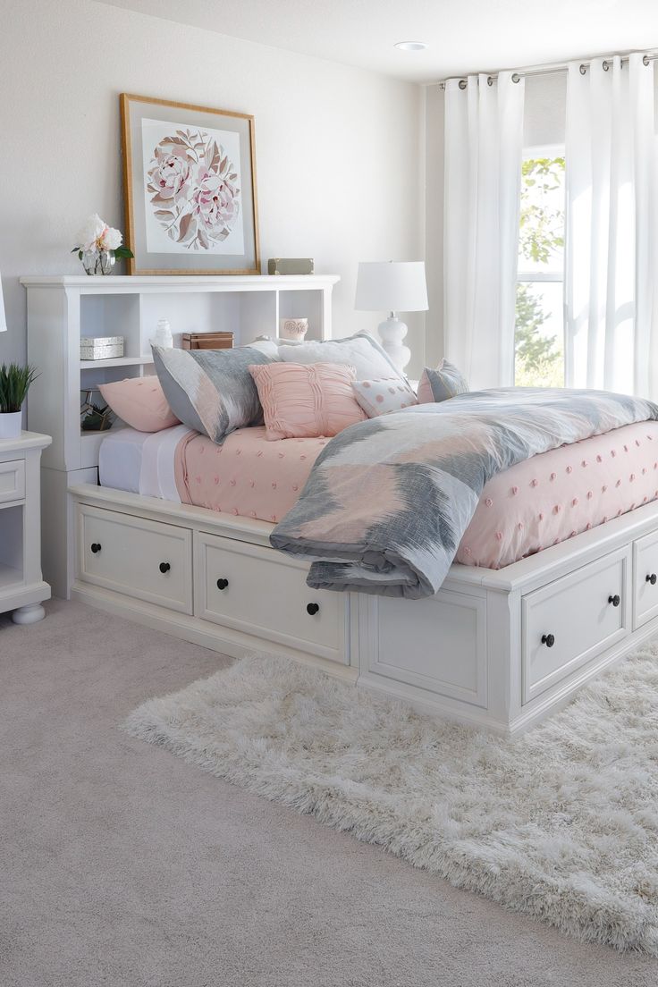 a white bed with pink and gray pillows