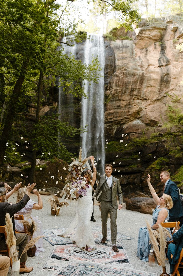 a bride and groom are walking down the aisle to their wedding ceremony under a waterfall