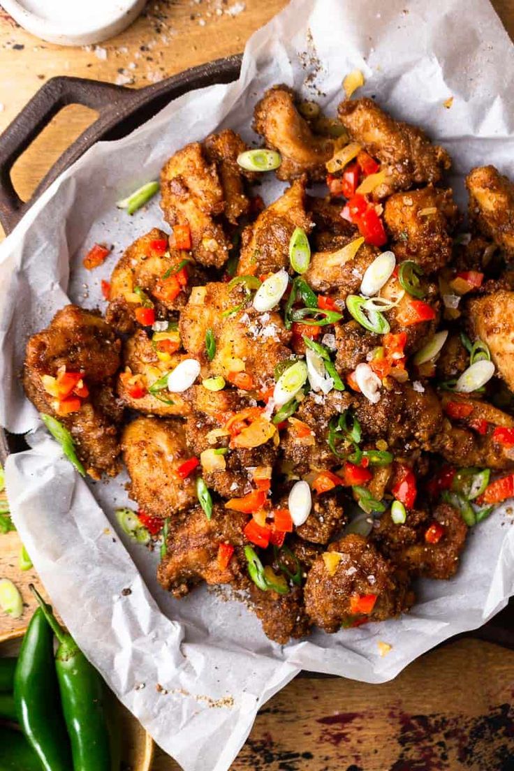 a plate filled with fried food on top of a wooden table next to green peppers