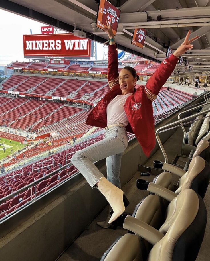 a woman is standing on the bleachers at a football stadium and holding her arms up