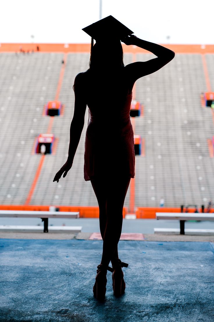 the silhouette of a woman wearing a graduation cap stands in front of an empty stadium