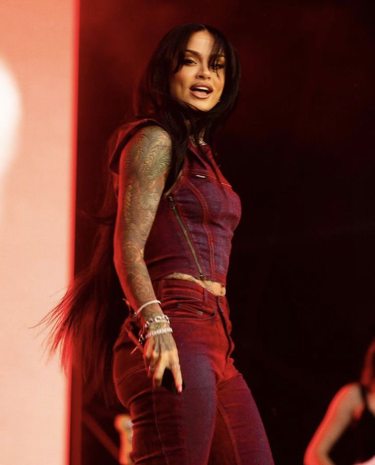 a woman with long hair and tattoos on her arm is standing in front of a microphone