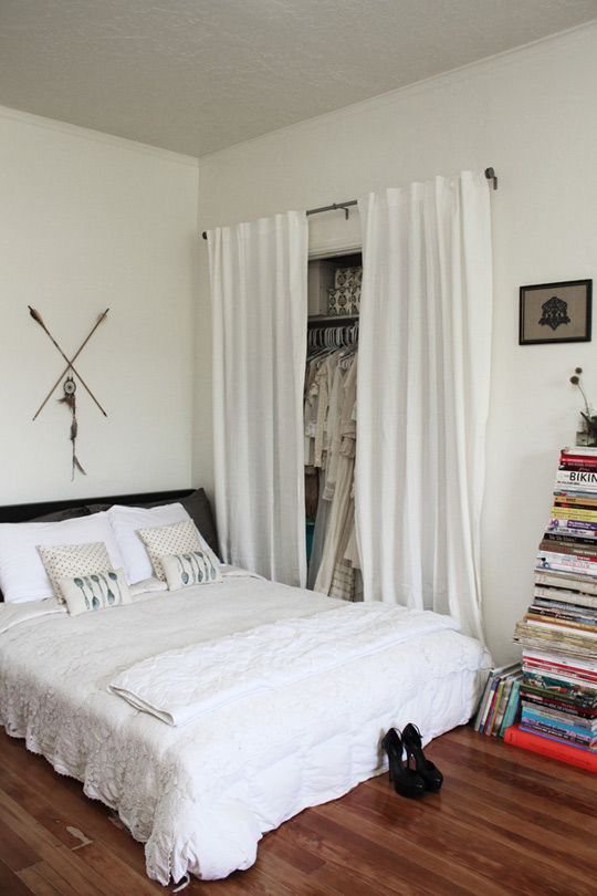 a white bed sitting in a bedroom next to a window covered in curtains and pillows