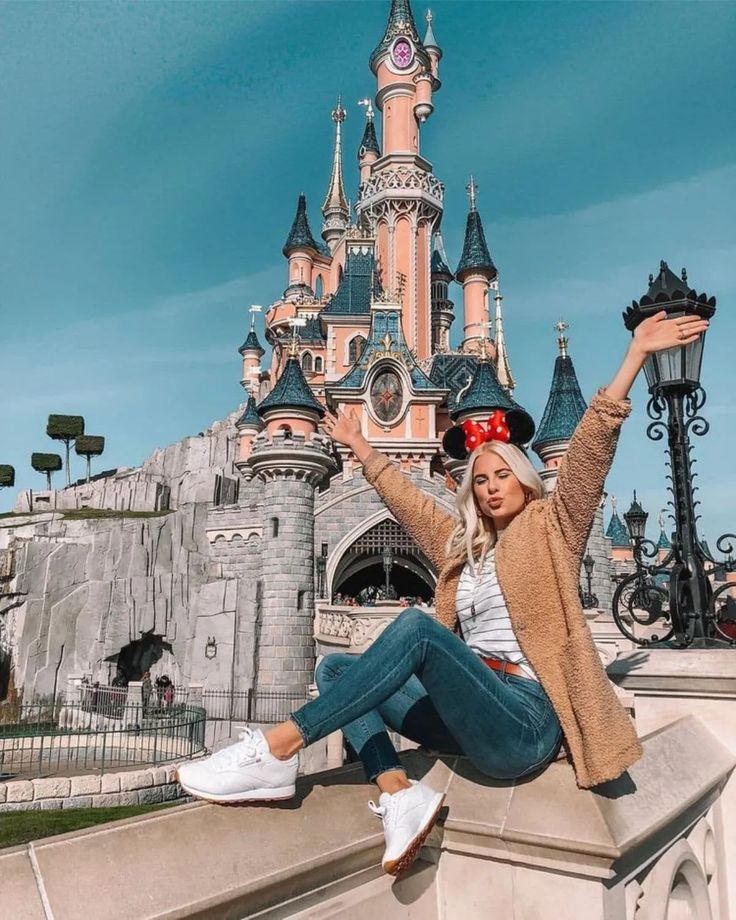 a woman sitting on the edge of a stone wall in front of a disney castle