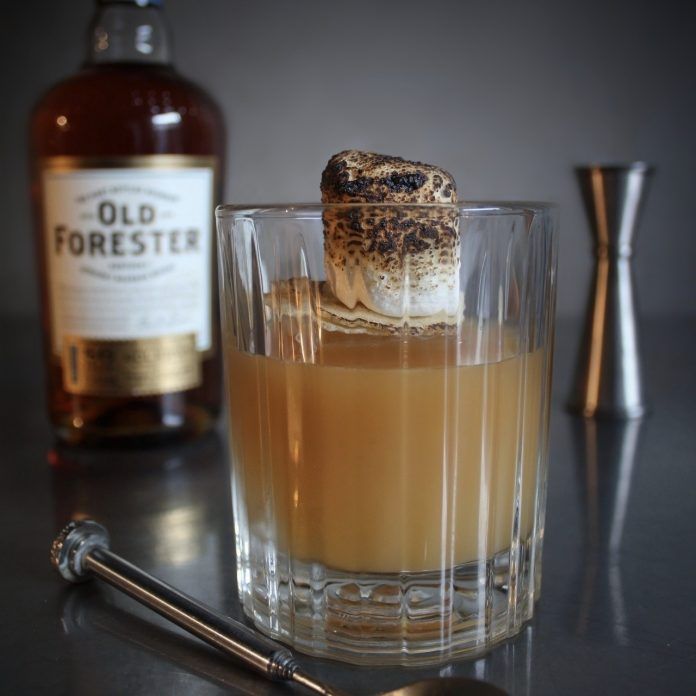 an old forester cocktail in a glass next to a bottle and spoon on a table