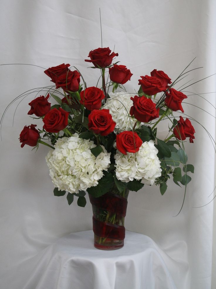 a vase filled with red and white flowers on top of a tablecloth covered table