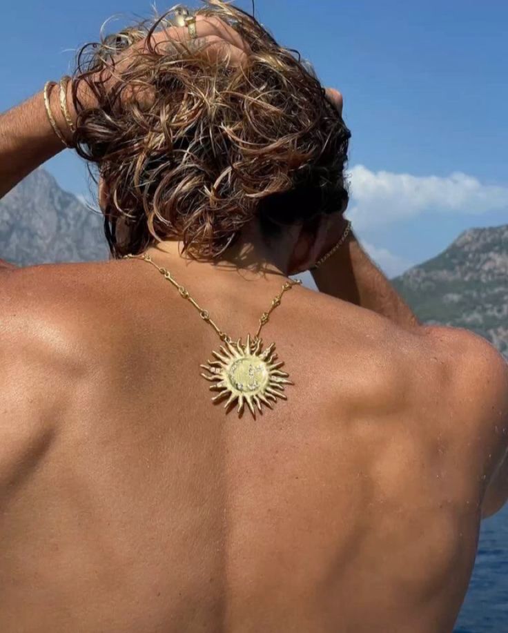 the back of a man wearing a gold sun necklace